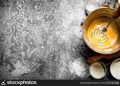 Baking background. Whisking fresh eggs in a bucket on a rustic background.
