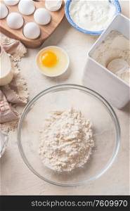 Baking background with flour in bowl, eggs and ingredients on white kitchen table background, top view. Home Bake. Recipes to cookies, pie and cake