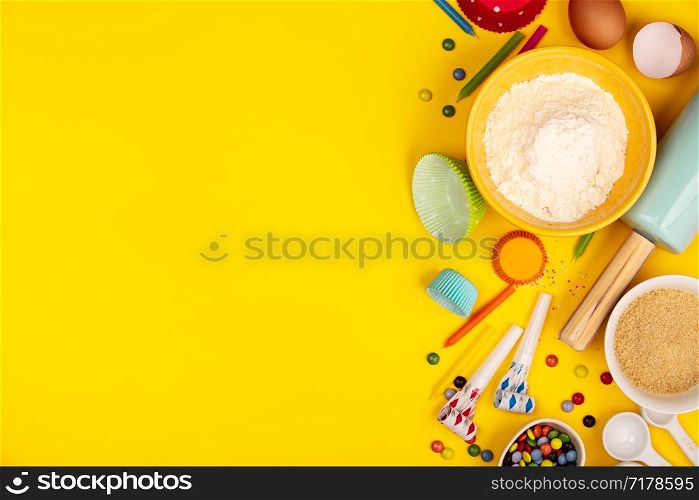 Baking birthday cupcakes background frame. Ingredients, kitchen items for baking, candles. Kitchen utensils, flour, eggs, sugar. Text space, top view.. Baking birthday cupcakes ingredients on yellow background, flat lay