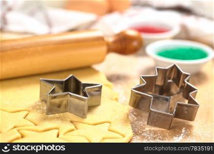 Baking Christmas Cookies: Cookie cutter on rolled out sugar or butter cookie dough with rolling pin and colorful sprinkles in the back (Selective Focus, Focus on the lower edges of the star- and tree-shaped cookie cutters) . Baking Christmas Cookies