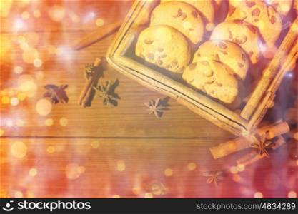 baking, christmas, holidays and food concept - close up of oat cookies in wooden box, and cinnamon on table over lights