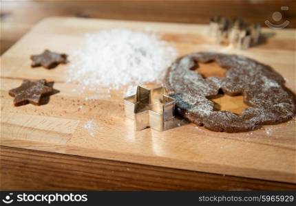 baking, cooking, christmas and food concept - close up of ginger dough, molds and flour on wooden cutting board from top