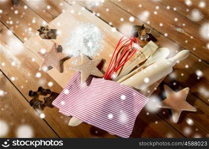 baking, cooking, christmas and food concept - close up of gingerbread cookies, molds with flour and kitchenware set on wooden cutting board at home kitchen from top