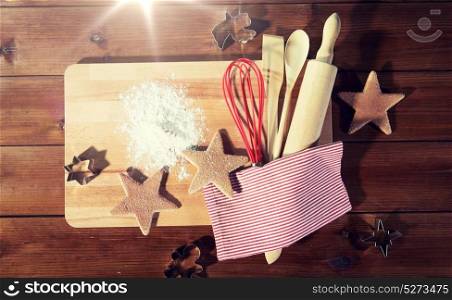 baking, cooking, christmas and food concept - close up of gingerbread cookies, molds with flour and kitchenware set on wooden cutting board at home kitchen from top. close up of gingerbread and baking kitchenware set