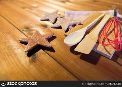 baking, cooking, christmas and food concept - close up of gingerbread cookies, kitchenware set and towel on wooden cutting board at home kitchen