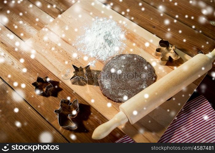 baking, cooking, christmas and food concept - close up of gingerbread dough, metal molds and rolling pin with flower on wooden cutting board at home kitchen from top