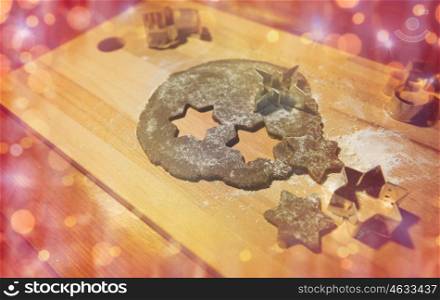 baking, cooking, christmas, holidays and food concept - gingerbread dough and molds on wooden cutting board over lights