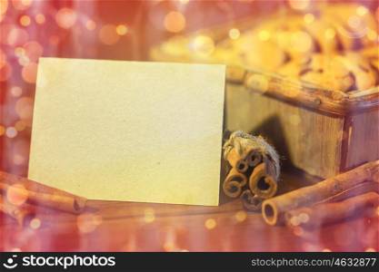 baking, culinary, christmas, holidays and food concept - close up of blank greeting card with oat cookies in wooden box and cinnamon over lights