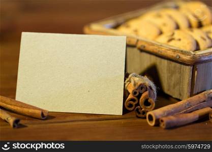 baking, culinary, holidays and food concept - close up of blank greeting card with oat cookies in wooden box and cinnamon on table