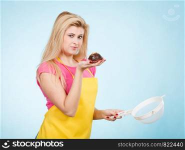 Baking tasty desserts sweets at home concept. Blonde woman holding delicious chocolate cupcake and colander. Woman holding chocolate cupcake and colander
