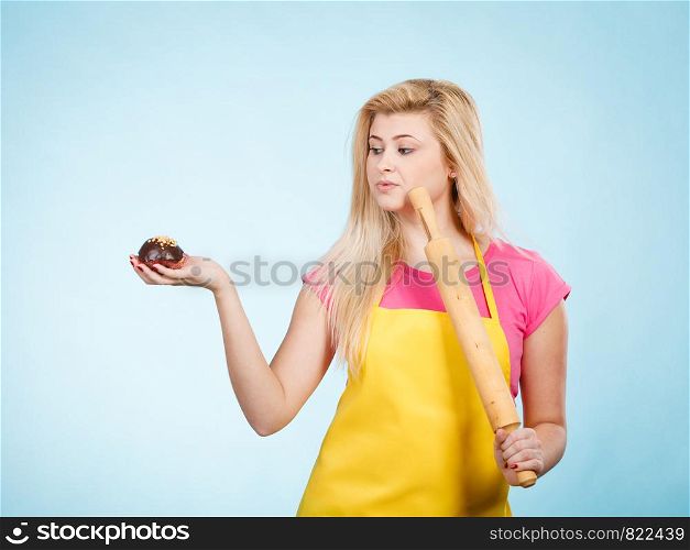 Baking tasty desserts sweets at home concept. Woman holding delicious chocolate cupcake and rolling pin wearing yellow apron.. Woman holding cupcake and rolling pin wearing apron