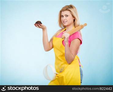 Baking tasty desserts sweets at home concept. Woman holding delicious chocolate cupcake, rolling pin and colander, wearing apron. Woman holding cupcake, rolling pin, colander wearing apron