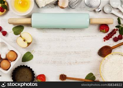 Baking tools and ingredients - flour, rolling pin, eggs, measuring spoons, fruits and berries on vintage wood table. Top view. Rustic background with free text space