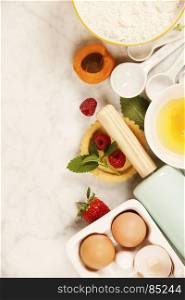 Baking tools and ingredients - flour, rolling pin, eggs, measuring spoons, fruits and berries on vintage wood table. Top view. Rustic background with free text space