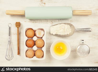 Baking tools and ingredients - flour, rolling pin, eggs, measuring spoons on vintage wood table. Top view. Rustic background with free text space