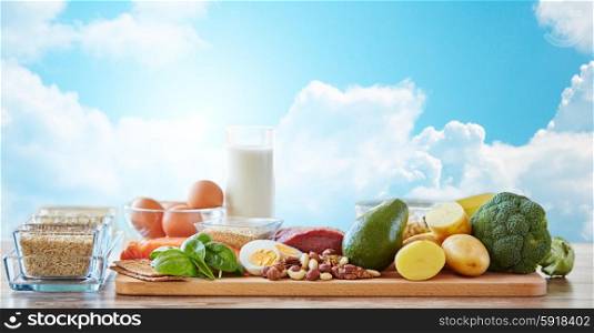 balanced diet, cooking, culinary and food concept - close up of vegetables, fruits and meat on wooden table over blue sky and clouds background