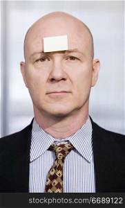 Bald businessman in with a blank sticky note on his forehead