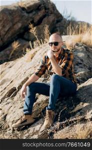 bald guy with a beard in jeans warm shirt and trekking shoes on granite rocks