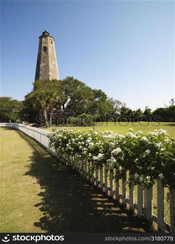 Bald Head Lighthouse with fence and wild roses at Bald Head Island, North Carolina.