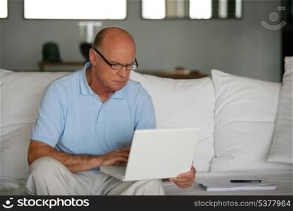 Bald man sat on sofa with laptop