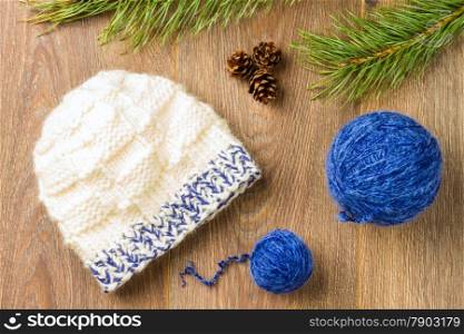 ball of threads, knitting cap, pine-cones and branch of pine on wooden background