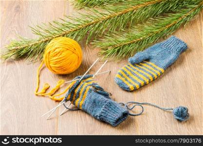 ball of threads, knitting needles, mittens and branch of pine on wooden background