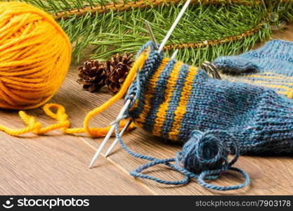 ball of threads, knitting needles, mittens and branch of pine on wooden background