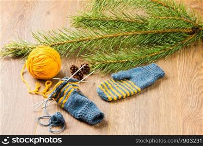 ball of threads, knitting needles, mittens and branch of pine on wooden background
