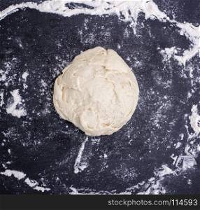 ball of wheat yeast dough on a black surface with flour, top view