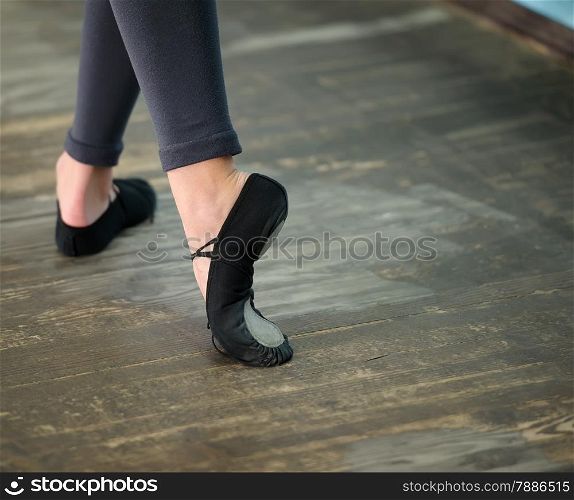 Ballerinas legs in black pointes on wooden floor in point position