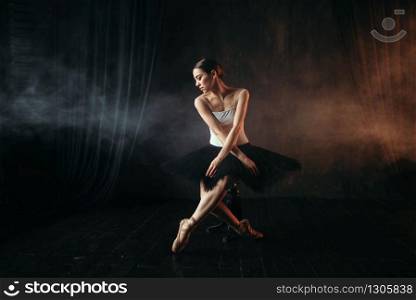 Ballet dancer sitting on black banquette on the stage in theatre. Graceful ballerina training in class. Ballet dancer sitting on black banquette