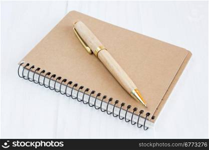 Ballpoint pen and brown cover notebook on wooden surface