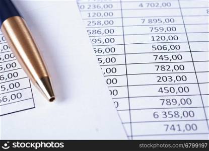 Ballpoint pen lying in a corner on printed financial tables. Pen laying on printed financial reports in the form of tables with numbers