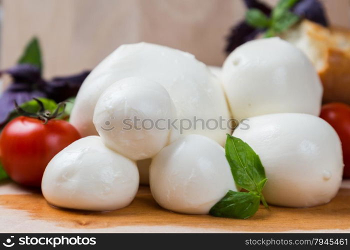 balls mozzarella different size with tomatoes cherry, bread and basil on wooden background