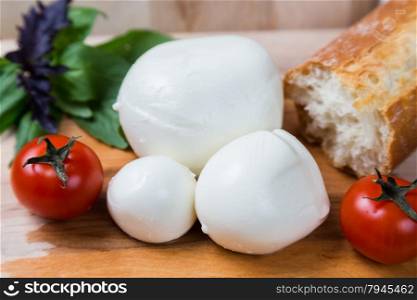 balls mozzarella different size with tomatoes cherry, bread and basil on wooden background