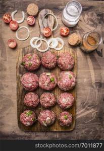 balls of minced meat on a cutting board with cherry tomatoes and seasonings on wooden rustic background top view close up
