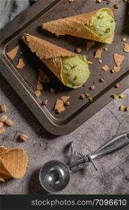 Balls of pistachio ice cream in waffle cones on a dark background.