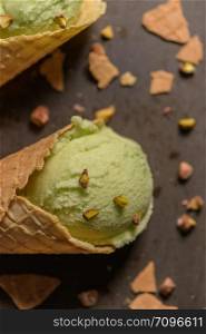 Balls of pistachio ice cream in waffle cones on a dark background.