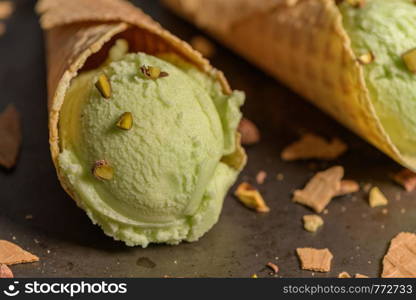 Balls of pistachio ice cream in waffle cones on a dark background.