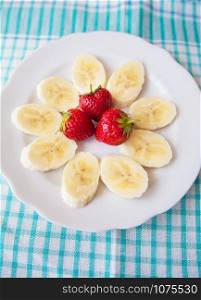 banana and strawberries on a white plate and a colorful napkin. banana and strawberries on white plate and a colorful napkin