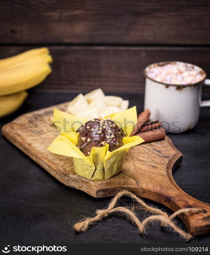 banana muffin wrapped in yellow paper on a wooden board, close up