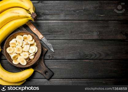 Bananas and banana pieces in a wooden plate on a cutting Board with a knife. On a black wooden background.. Bananas and banana pieces in a wooden plate on a cutting Board with a knife.