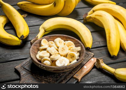 Bananas and banana pieces in a wooden plate on a cutting Board with a knife. On a black wooden background.. Bananas and banana pieces in a wooden plate on a cutting Board with a knife.