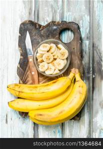 Bananas and banana slices in a glass bowl on an old cutting Board. On a white wooden background.. Bananas and banana slices in a glass bowl on an old cutting Board.