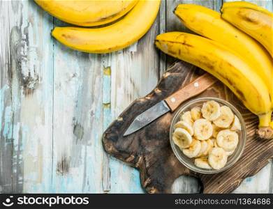 Bananas and banana slices in a glass bowl on an old cutting Board. On a white wooden background.. Bananas and banana slices in a glass bowl on an old cutting Board.