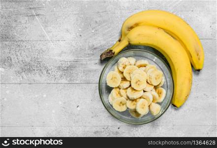 Bananas and banana slices in a glass plate. On white rustic background. Bananas and banana slices in a glass plate.