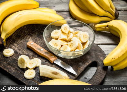 Bananas and banana slices in a plate on a black chopping Board with a knife. On a wooden background.. Bananas and banana slices in a plate on a black chopping Board with a knife.