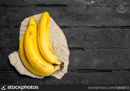 Bananas on grey paper. On a dark rustic background.. Bananas on grey paper.