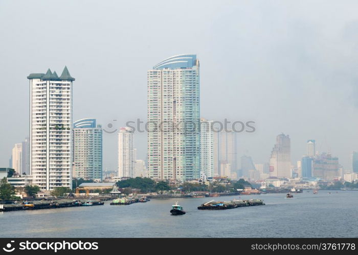 Bangkok city has a lot of tall buildings. Adjacent river boat traffic.