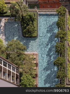 Bangkok, Thailand - 08 Jan 2021   Top down aerial view of outdoor swimming Pool surrounding palms and green garden in the beautiful condominium. Modern landscape architecture with swimming pool.